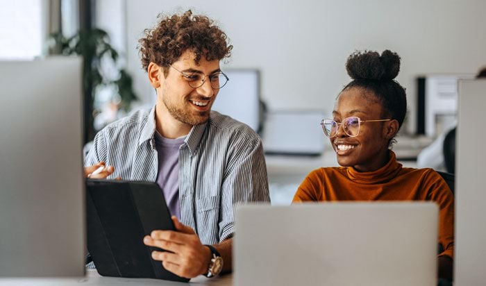 Two smiling coworkers looking at a laptop screen in an office