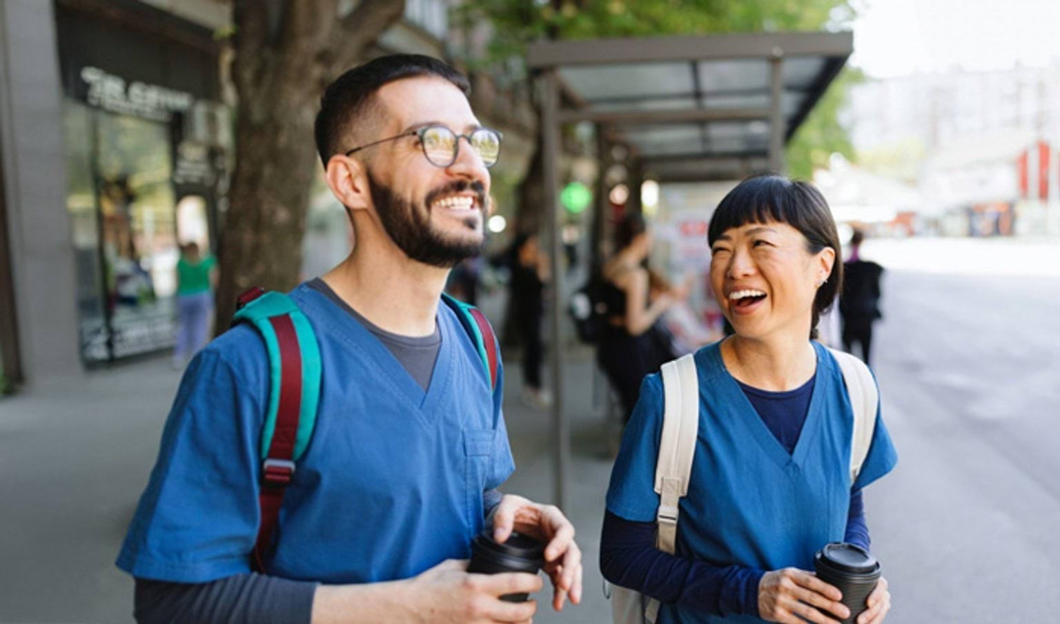A male and female hospital worker holding takeaway coffee and laughing together