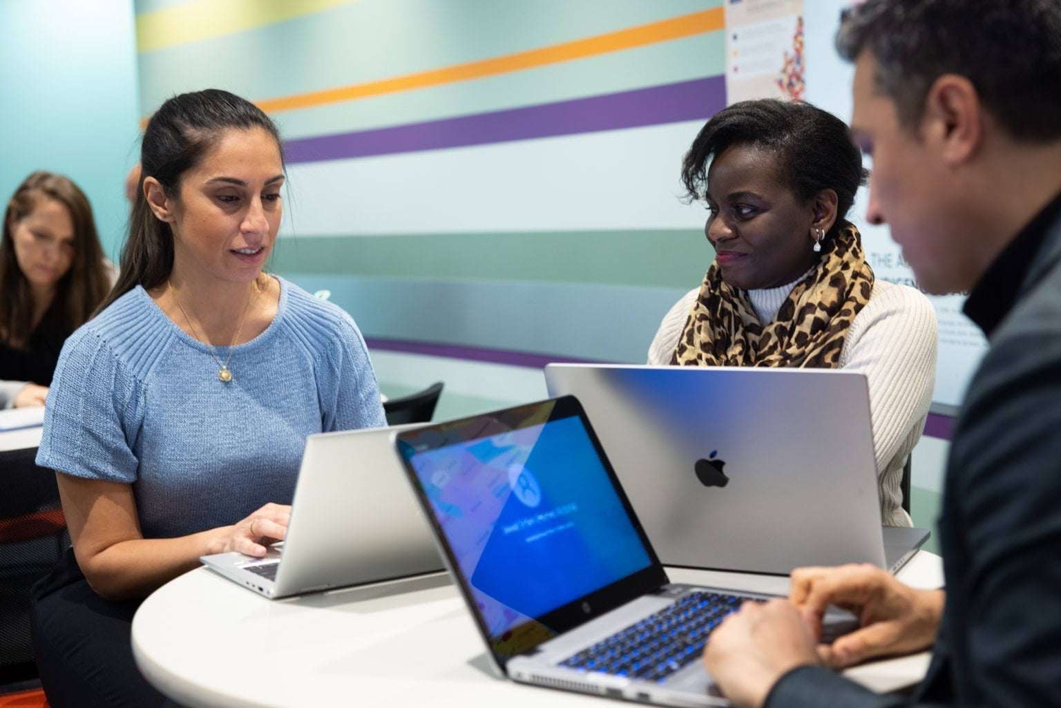 Three people collaborating at a table with laptops, in a colorful office setting