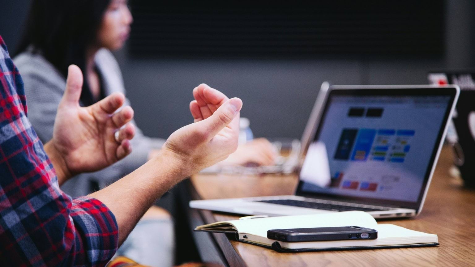 Laptop on table with man's hands open, explaining content.